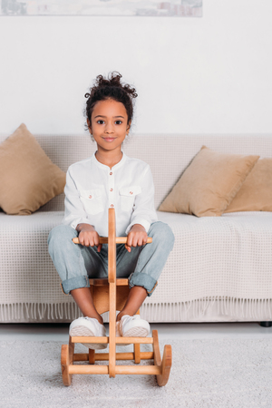 African american kid sitting on wooden rocking horse and looking at cameraの写真素材