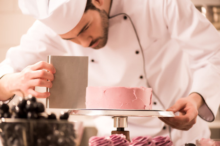Focused confectioner making sweet cake in restaurant kitchenの写真素材