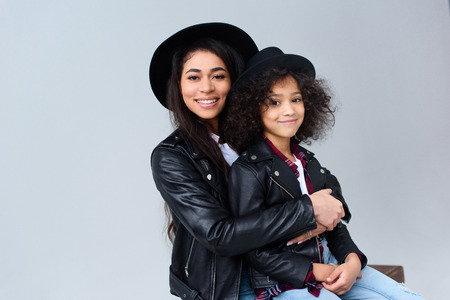 Happy mother and daughter embracing and looking at camera isolated on greyの写真素材