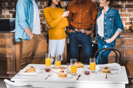 glasses of juice and tasty pancakes on table and young multiethnic friends standing behindの写真素材