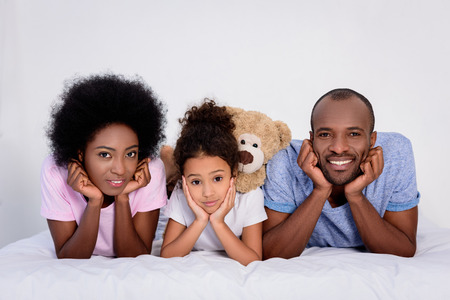 african american parents and daughter resting chins on hands at homeの写真素材