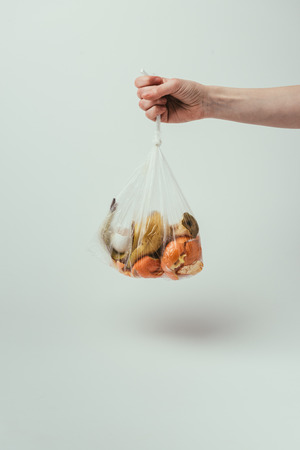 Cropped shot of woman holding plastic bag with trash on grey backgroundの写真素材
