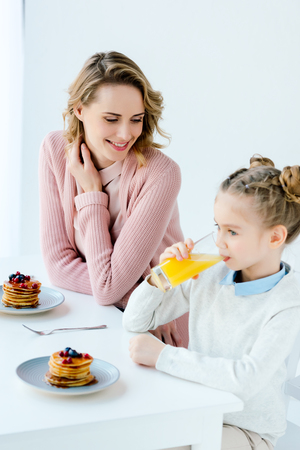 Smiling mother and daughter having breakfast together at tableの写真素材