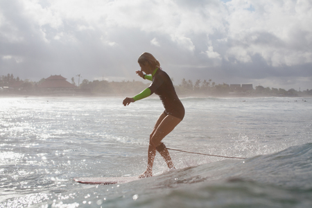 Silhouette of sportswoman riding wave on surf board in ocean with backlitの写真素材