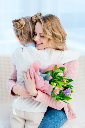 Happy mother hugging daughter and holding bouquet on happy mothers dayの写真素材