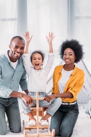 African american parents and daughter playing with rocking horse at homeの写真素材