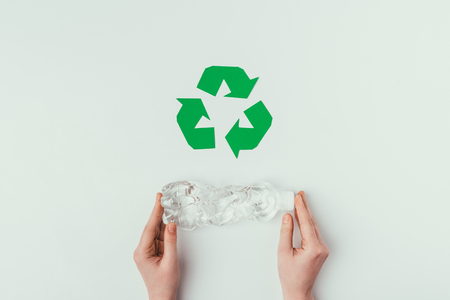 Partial view of woman holding plastic bottle with recycle sign isolated on greyの写真素材