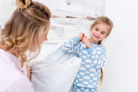 Mother and daughter having fun and fighting with pillows at homeの写真素材