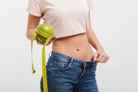 cropped shot of woman holding apple tied with measuring tape isolated on whiteの写真素材