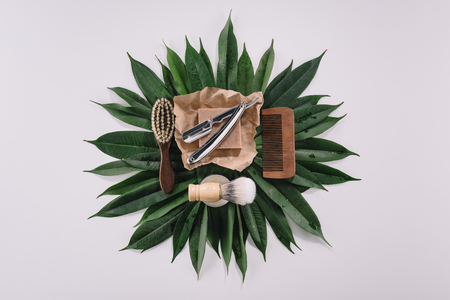 top view of arranged barber tools for shaving on green leaves isolated on greyの写真素材