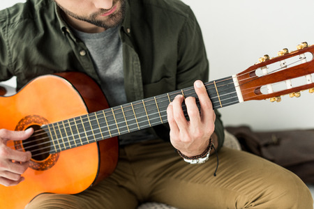 cropped image of man playing barre chord on acoustic guitarの写真素材