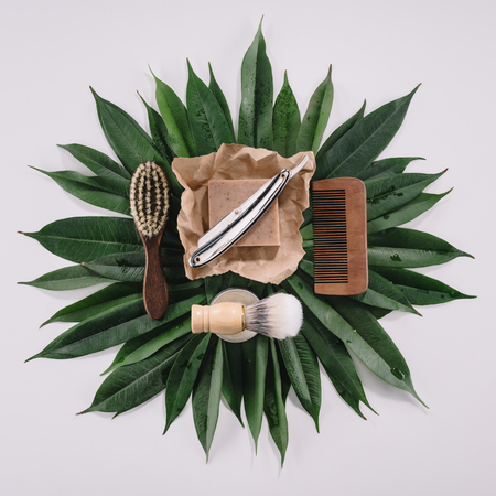 top view of arranged barber tools for shaving on green leaves isolated on greyの写真素材
