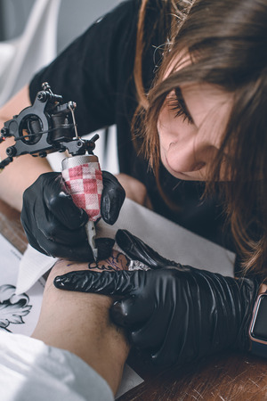 Female tattoo master in gloves with machine working on arm pieceの写真素材