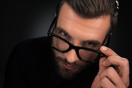 portrait of man in eyeglasses looking at camera isolated on blackの写真素材