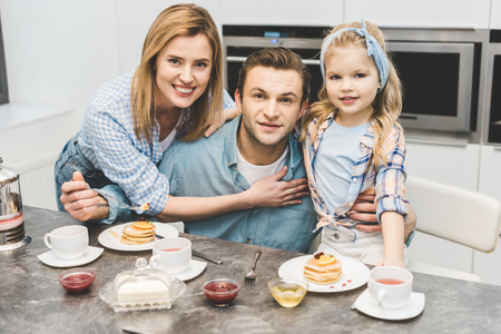 portrait of smiling parents and daughter looking at camera during breakfast at homeの写真素材