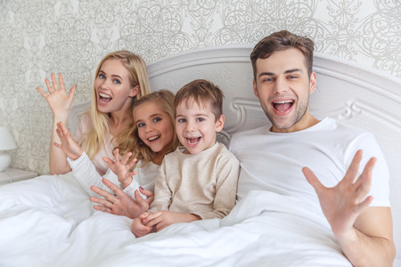young family relxing in bed together on weekend morningの写真素材