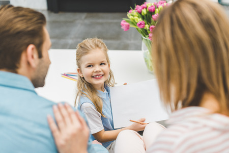 selective focus of smiling daughter showing blank paper to parents at homeの写真素材