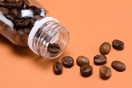 close up view of roasted coffee beans and plastic bottle isolated on peachの写真素材