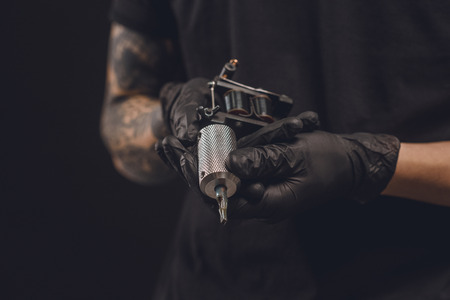 Male hands in gloves holding tattoo machine isolated on blackの写真素材