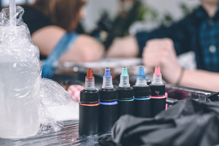 Bottles of ink on table in front of working tattoo artistの写真素材