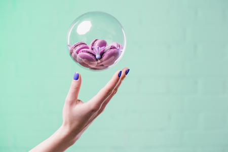 cropped shot of woman throwing up glass ball with macarons on turquoiseの写真素材