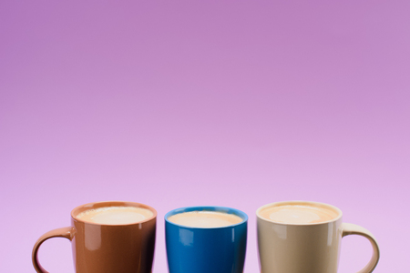 close up view of arranged colorful cups of coffee isolated on purpleの写真素材
