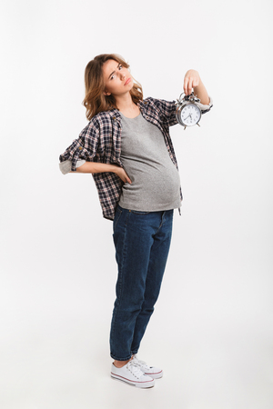 sad pregnant woman with clock in hand isolated on greyの写真素材