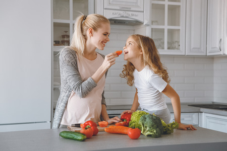 smiling pregnant mother giving daughter piece of bell pepperの写真素材