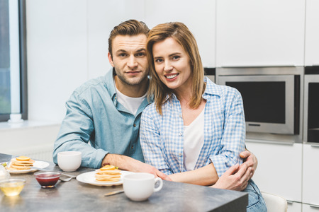 portrait of smiling couple sitting at table with breakfast at homeの写真素材