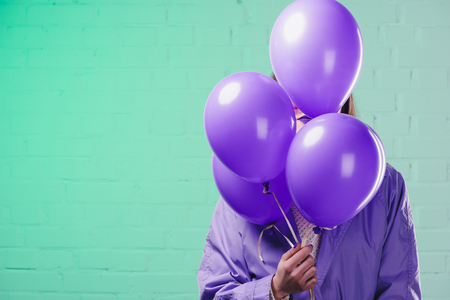 young woman in coat hiding behind purple helium balloonsの写真素材