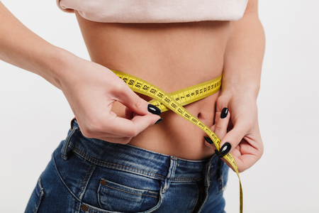 cropped shot of woman measuring her waist with tape isolated on whiteの写真素材