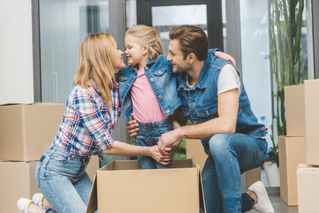 portrait of smiling parents and little daughter in cardboard box at new home, moving home concept