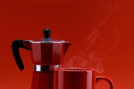 close up view of red cup of coffee and coffee maker isolated on redの写真素材