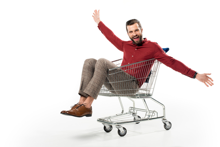 cheerful man sitting in shopping cart isolated on whiteの写真素材