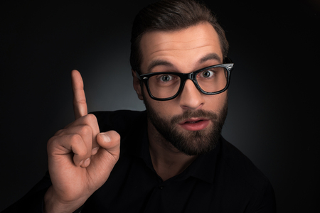 portrait of man in eyeglasses pointing up isolated on blackの写真素材