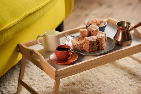 close up view of cup of coffee, jag of cream, pieces of cake and brown sugar on wooden tray in room