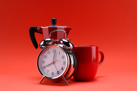 close up view of coffee maker, alarm clock and cup of coffee isolated on redの写真素材