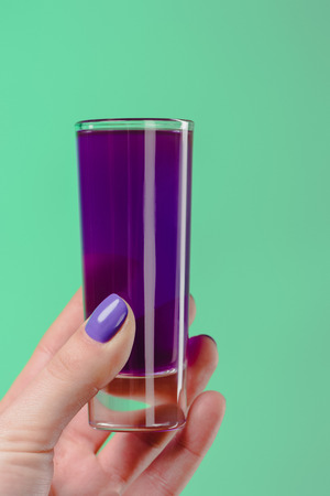 cropped image of woman holding glass with purple cocktail isolated on turquoiseの写真素材
