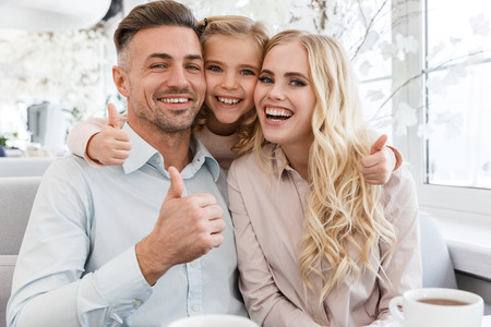 happy young family sitting in cafe and showing thumbs upの写真素材