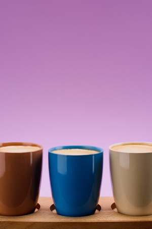 close up view of colorful cups of coffee isolated on purpleの写真素材