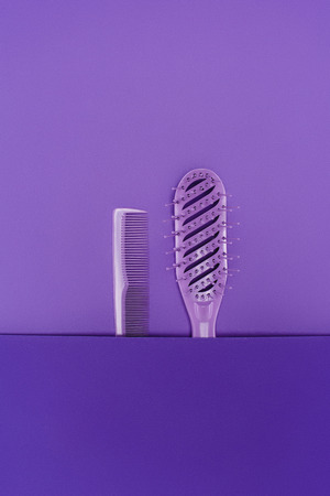 close up view of purple hairbrush and comb isolated on purpleの写真素材