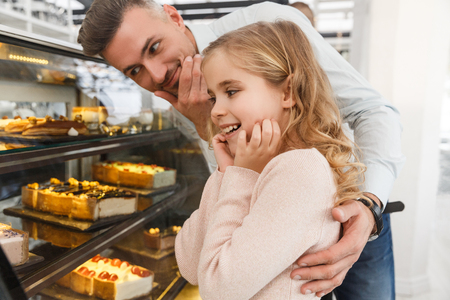 father and little daughter choosing cake on display at cafeの写真素材