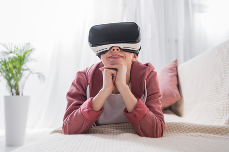 girl lying on sofa and watching something with virtual reality headset at home