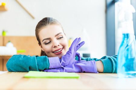 smiling young woman wearing rubber gloves while cleaning house