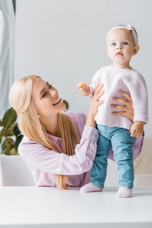 young mother looking at small cute daughter with cookieの写真素材