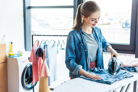 beautiful smiling young woman ironing clothes at homeの写真素材