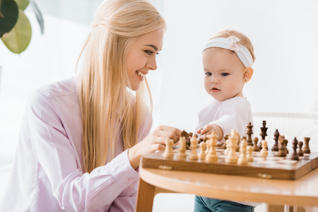 young cheerful mother teaching daughter playing chessの写真素材