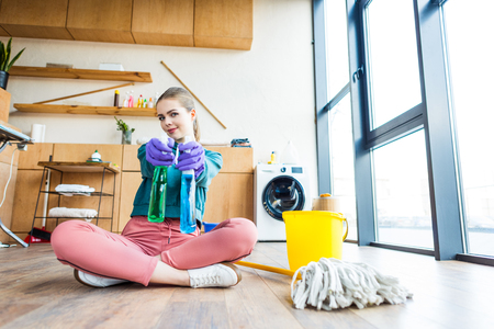 young woman in rubber gloves holding plastic bottles with cleaning fluids and smiling at cameraの写真素材