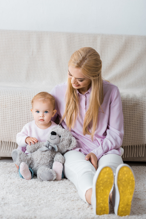 young woman sitting on floor with daughter and teddy bearの写真素材