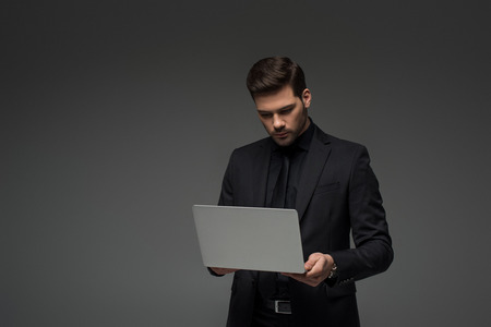 stylish businessman holding laptop isolated on greyの写真素材
